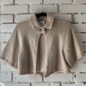 Cream cropped cape shrug cardigan in wool with button closure at neck.